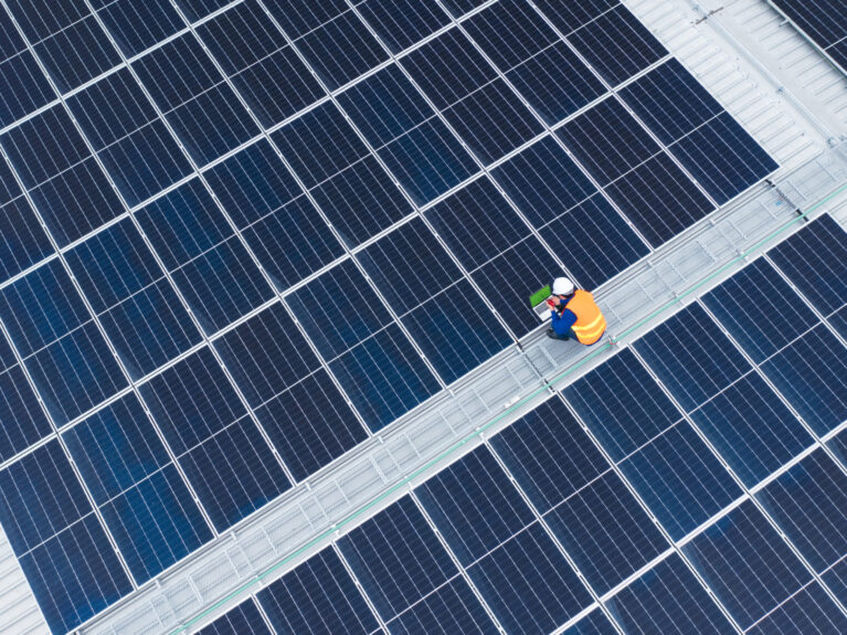 High Angle View of Engineer with laptop and radio communication working on solar panels,He works on the rooftop under sunlight