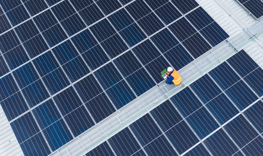 High Angle View of Engineer with laptop and radio communication working on solar panels,He works on the rooftop under sunlight