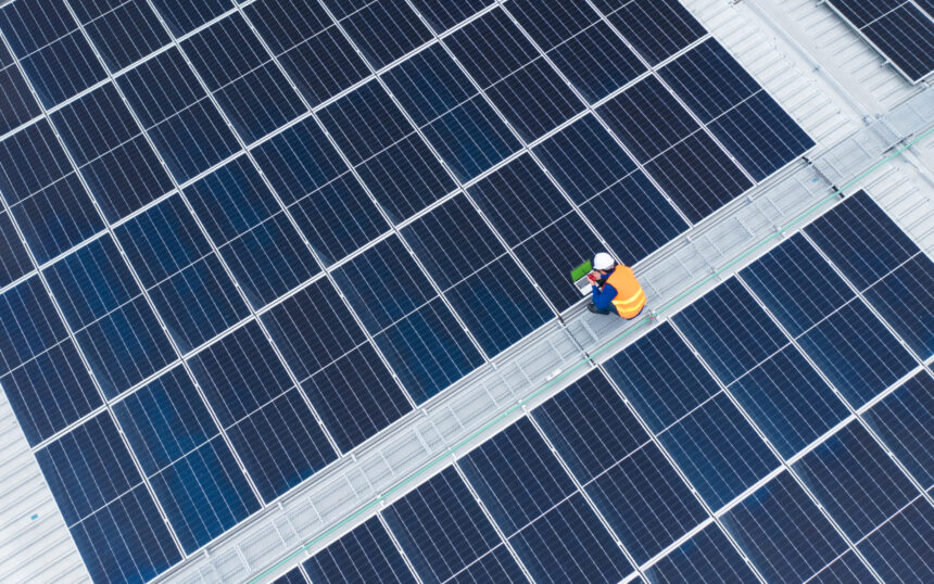 High Angle View of Engineer with laptop and radio communication working on solar panels,He works on the rooftop under sunlight
